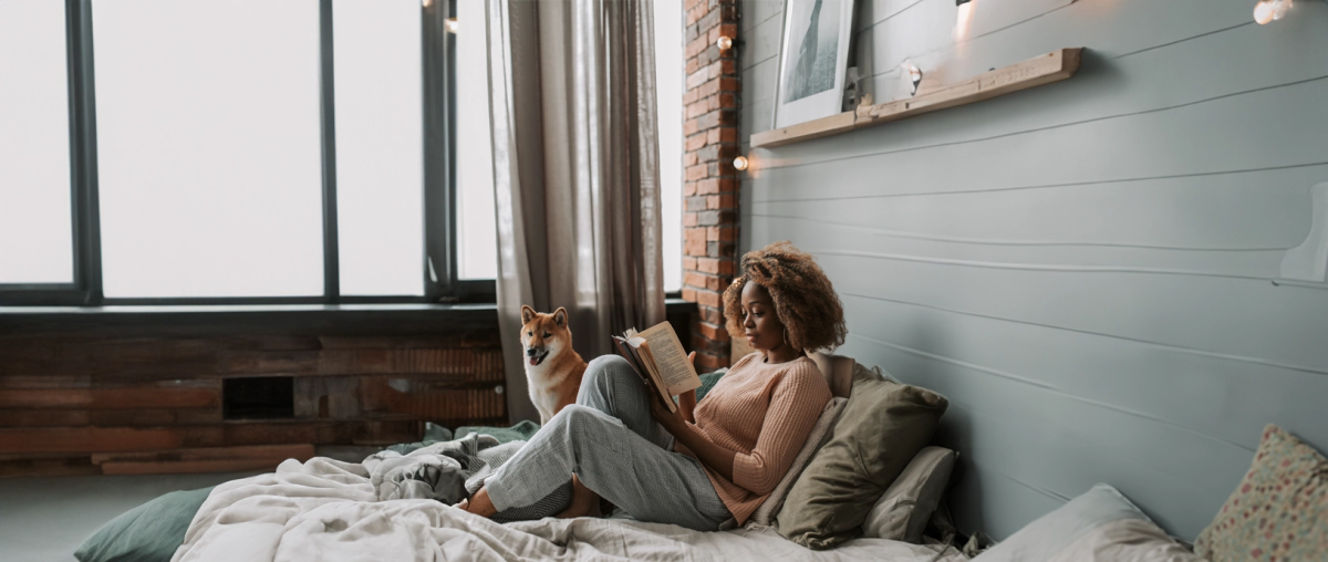 Een vrouw ligt op bed en leest een boek. Haar hond ligt naast haar en slaapt.